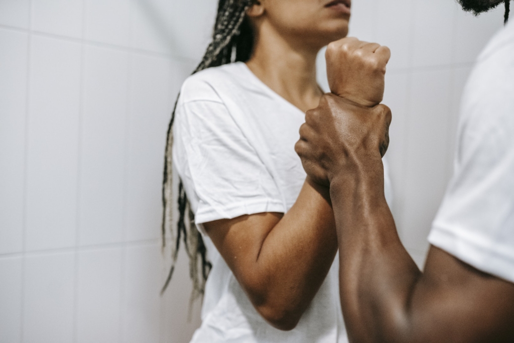 Side view of crop unrecognizable aggressive African American male holding wrist of scared wife while quarreling together in bathroom